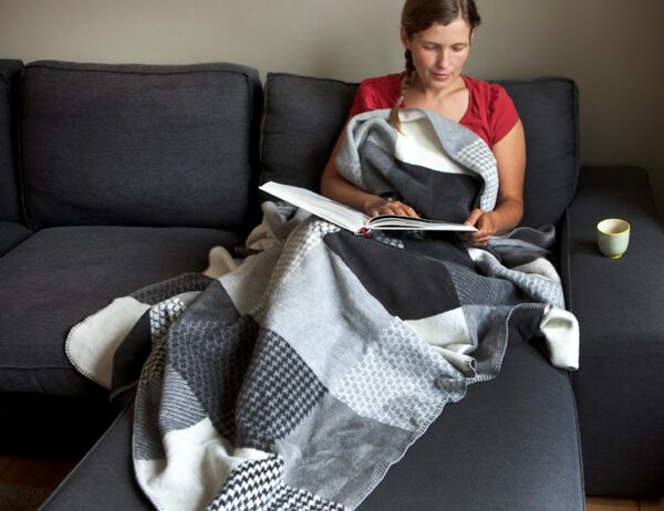 Frau in Decke gekuschelt, sitz gemütlich auf einer Couch
